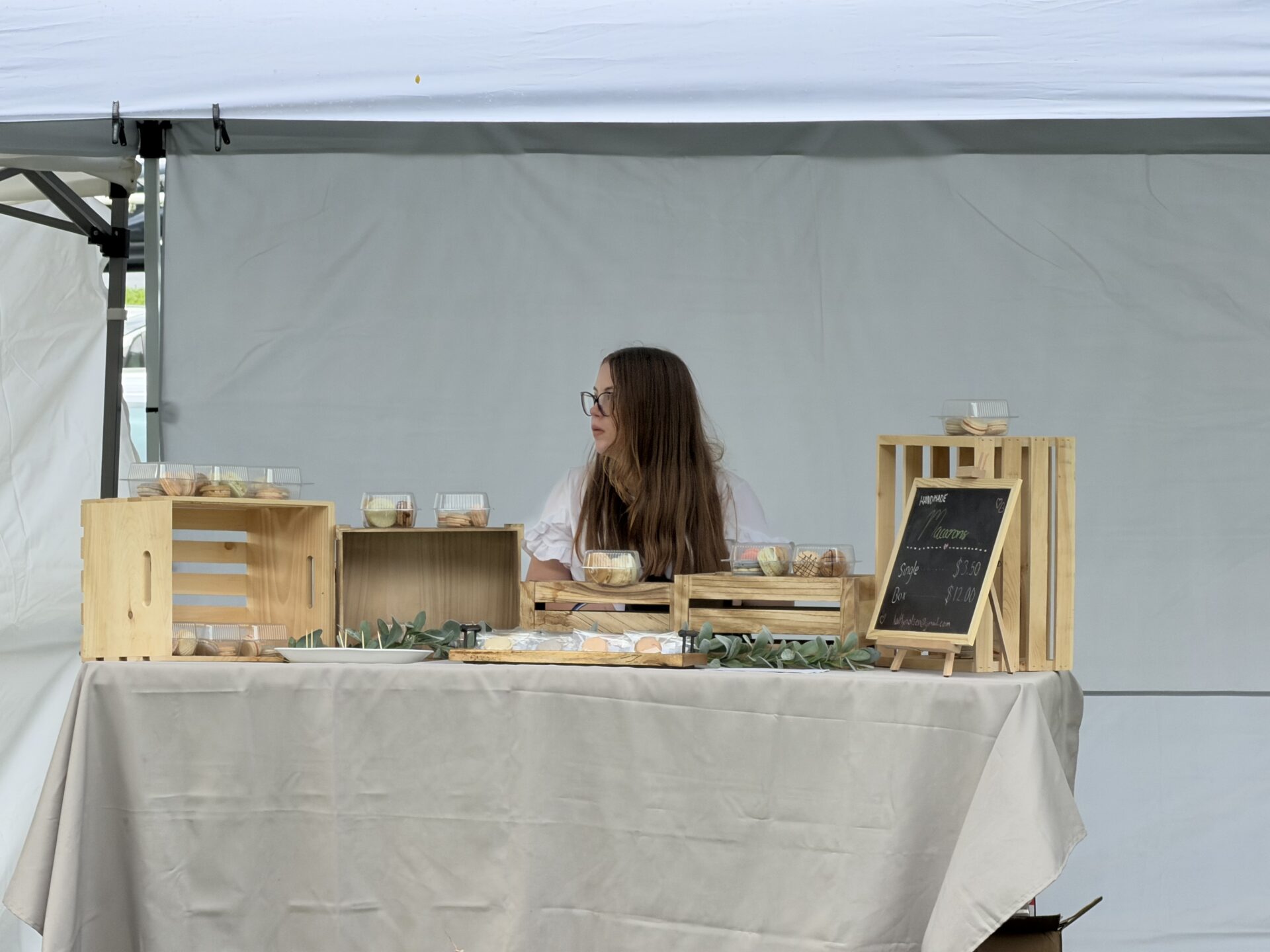 Kaitlyn standing behind her handmade macaron booth at the farmers market