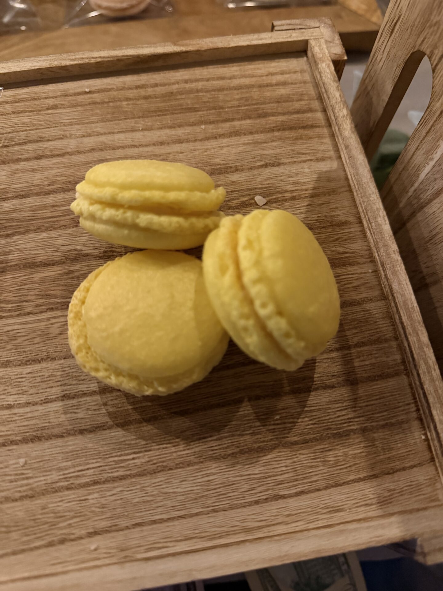 Three yellow handmade macarons on a wooden serving tray